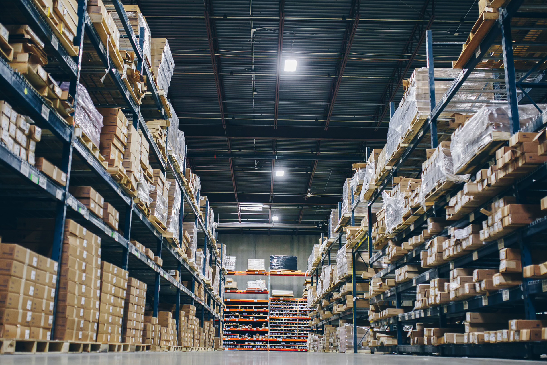 Warehouse aisle with tall shelves full of stacked cardboard boxes.