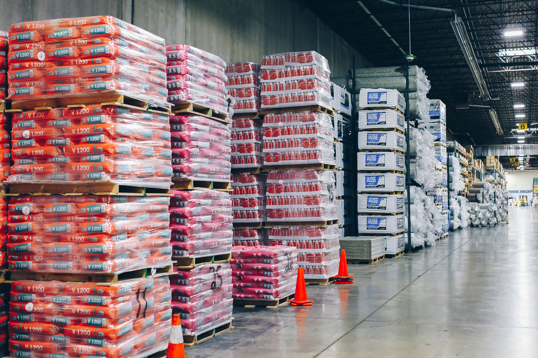 Warehouse with stacked pallets of construction materials and safety cones.
