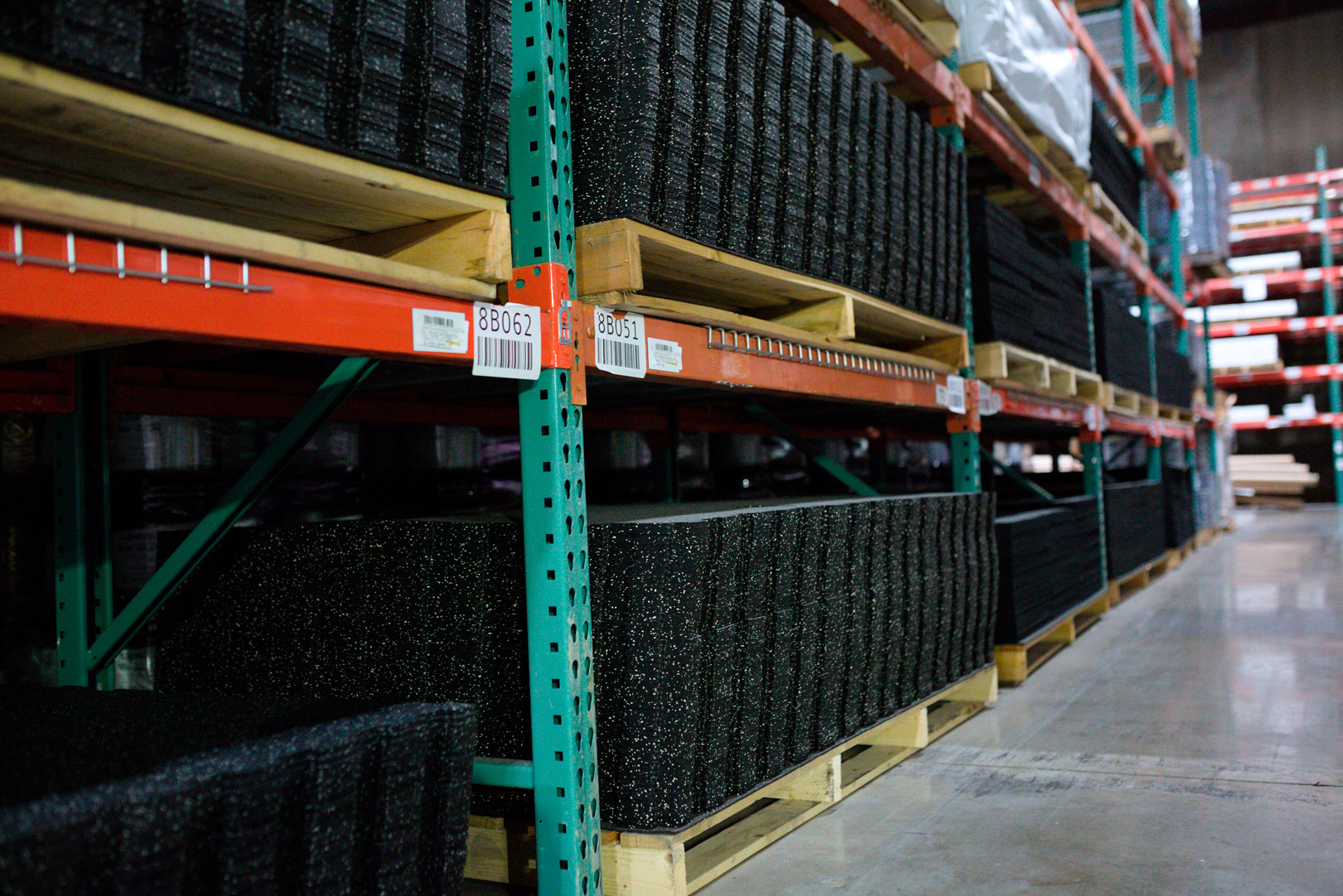 Warehouse shelves with stacked black rubber mats on pallets.