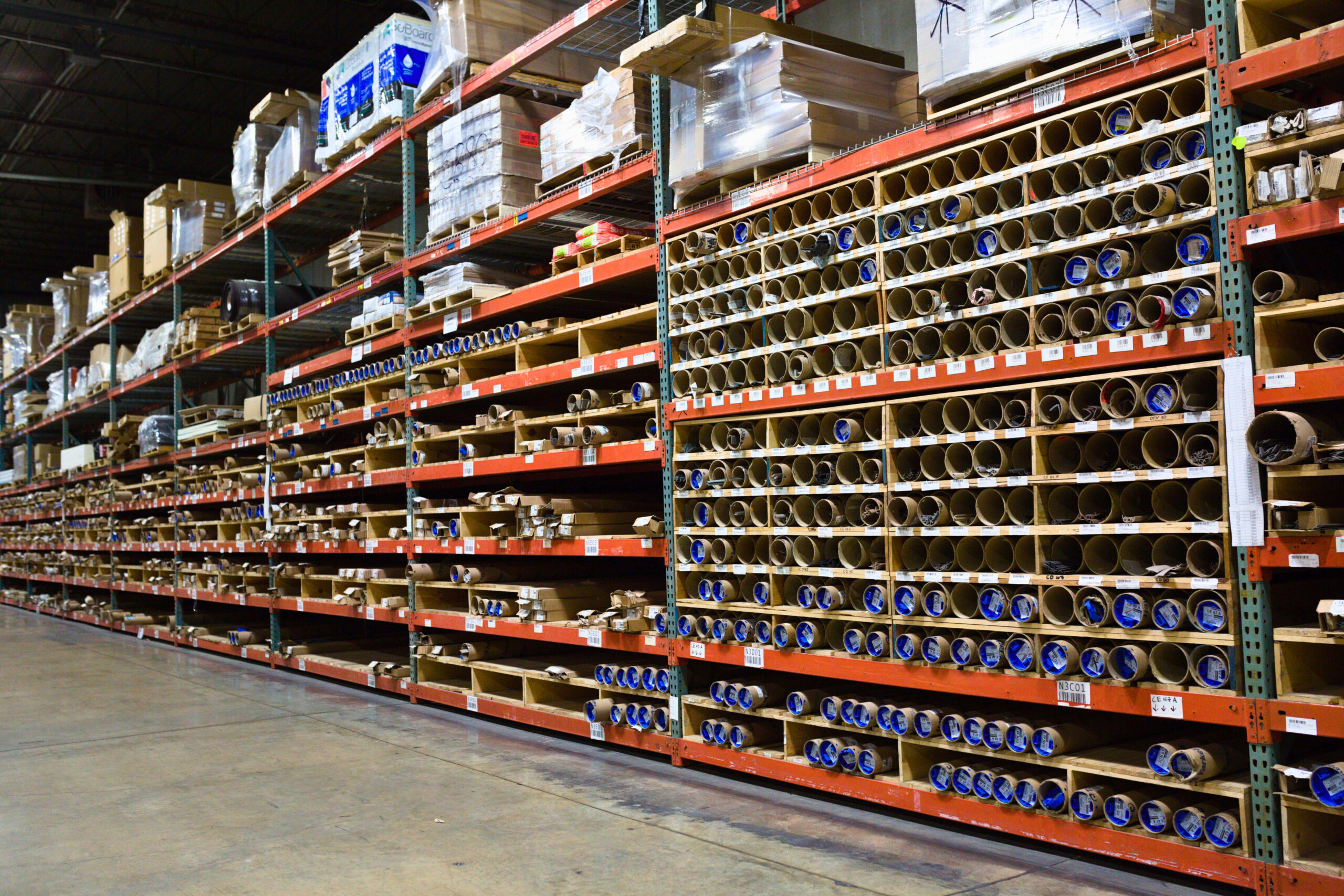 Long warehouse shelving with labeled cardboard storage tubes and boxes.